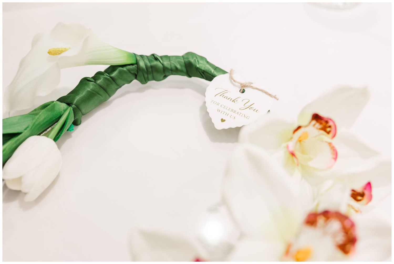 White tulip bouquet wrapped in green ribbon with a thank you tag, surrounded by white orchids.