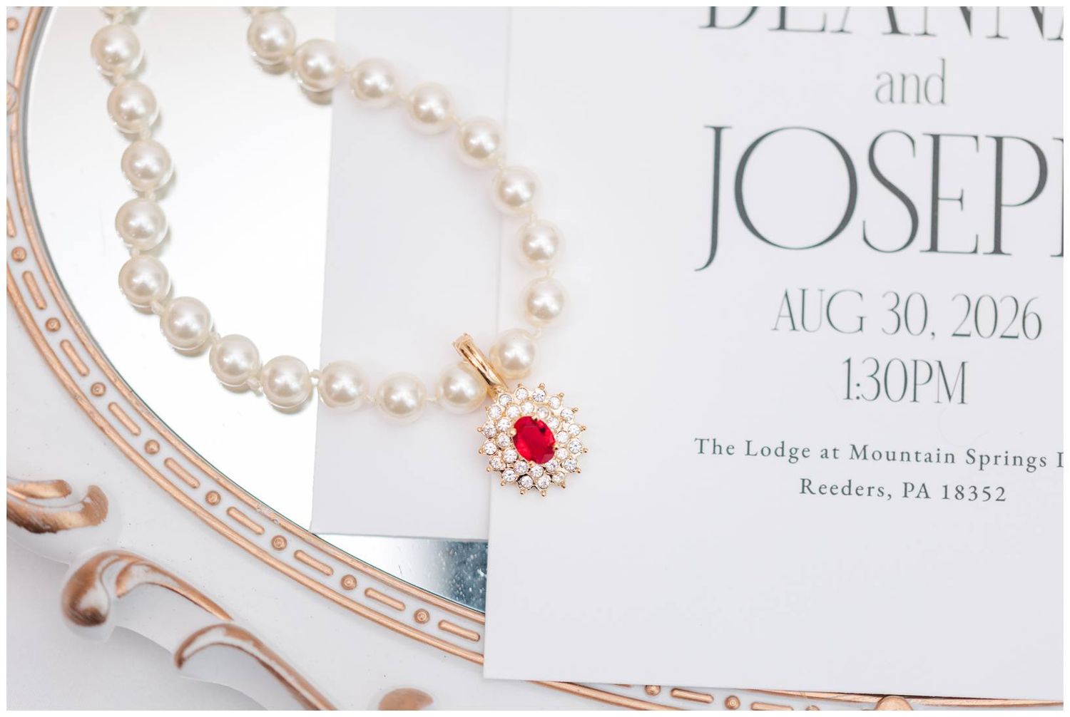 Pearl necklace with ruby pendant on wedding invitation for Deanna and Joseph, August 30, 2026, at The Lodge at Mountain Springs.