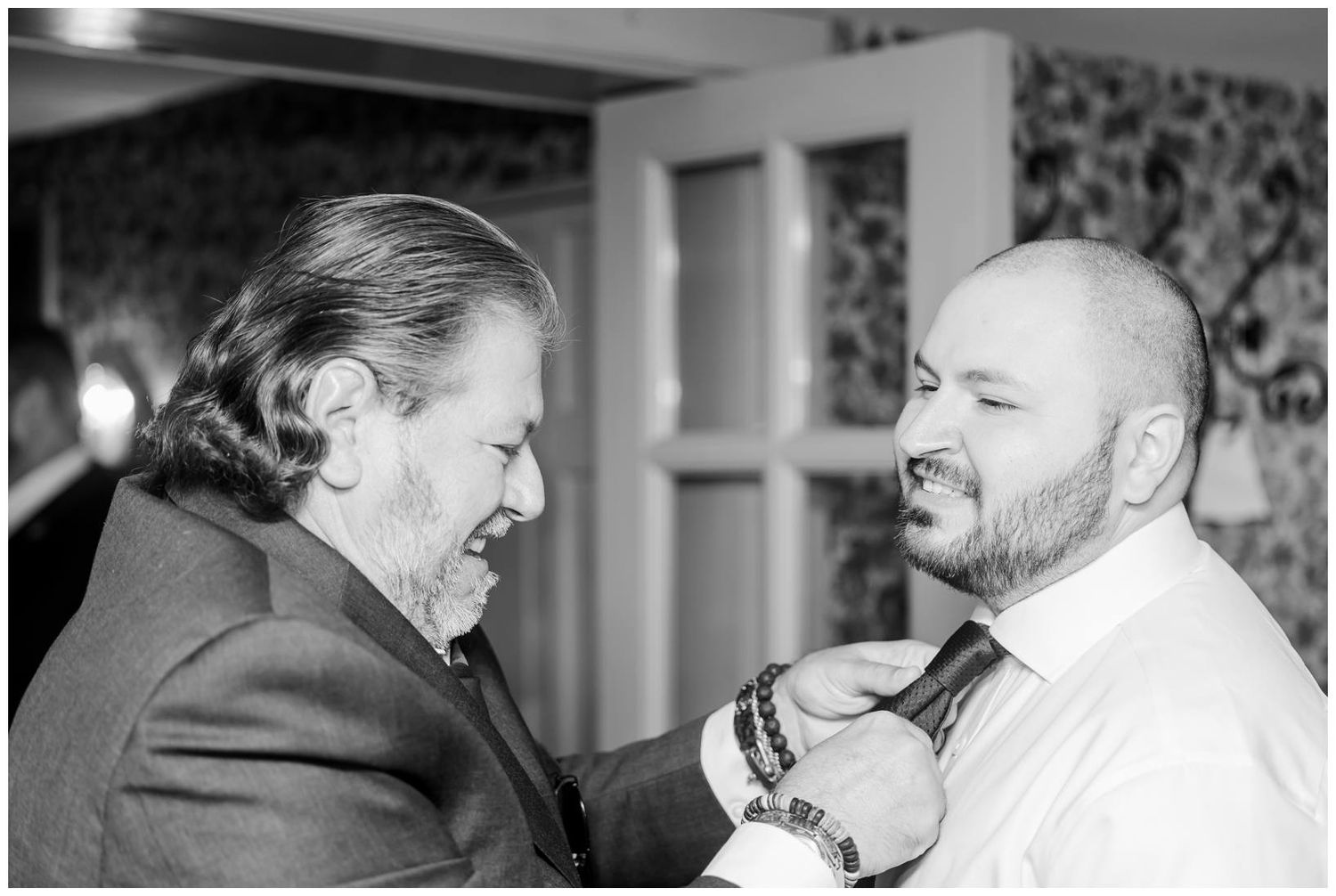Black and white photo of two men adjusting a tie, likely a father helping groom prepare before wedding ceremony.