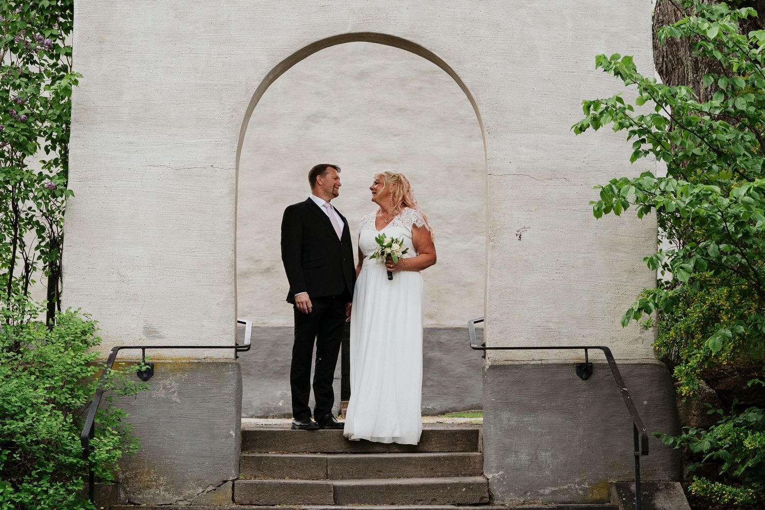 Brudpar står tillsammans vid en vacker byggnad under sin bröllopsfotografering i Kungsgården