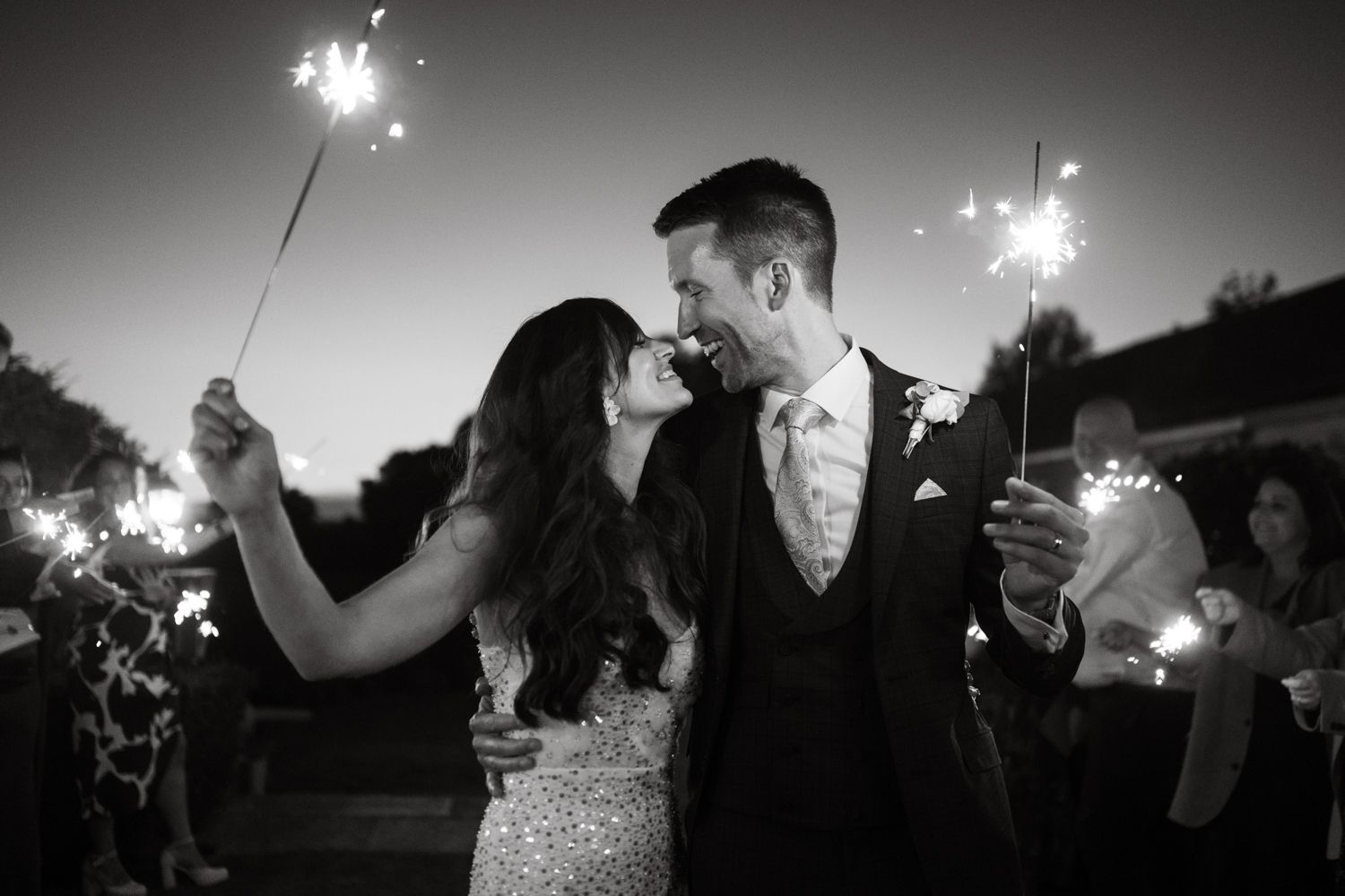 Black and white photo of a bride and groom sharing a romantic moment while holding sparklers at their wedding reception.