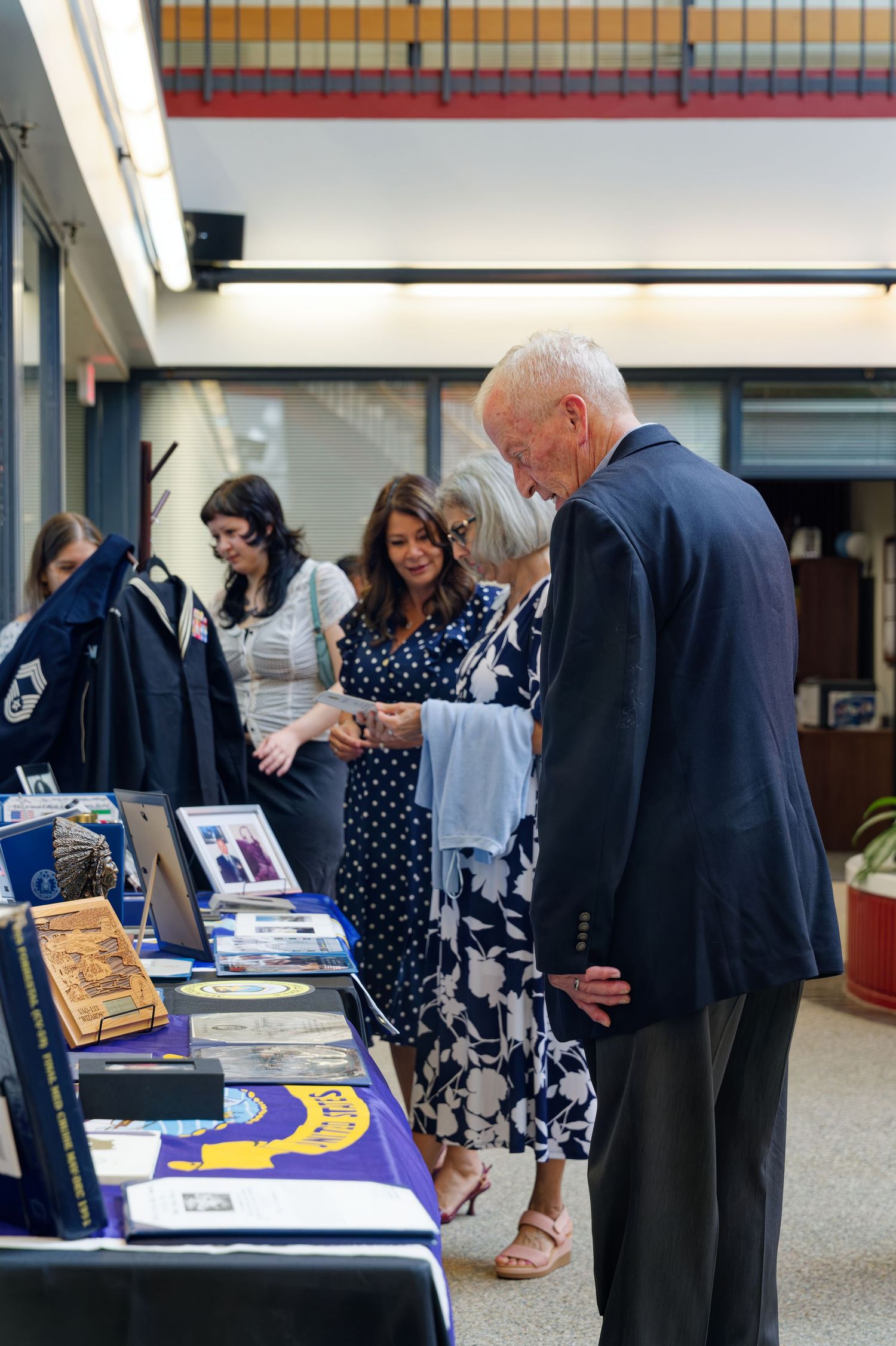 Visitors browsing military memorabilia display tables at an indoor veterans recognition ceremony event.