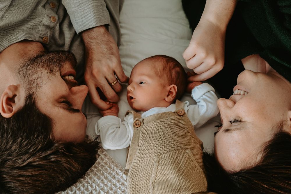Two parents lying down with their newborn baby between them, sharing a tender family moment.