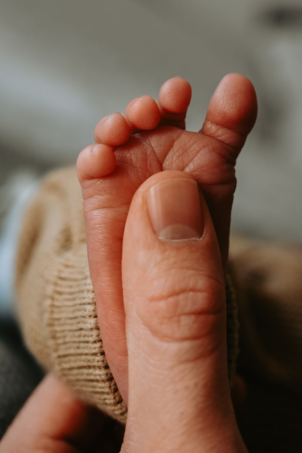 Close-up of an adult hand gently holding a tiny newborn baby foot, showcasing delicate toes and soft skin.