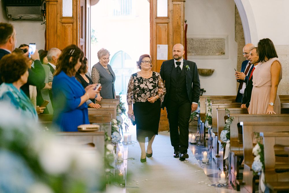 Arrivo della sposa tra persone e fiori, davanti all’ingresso.