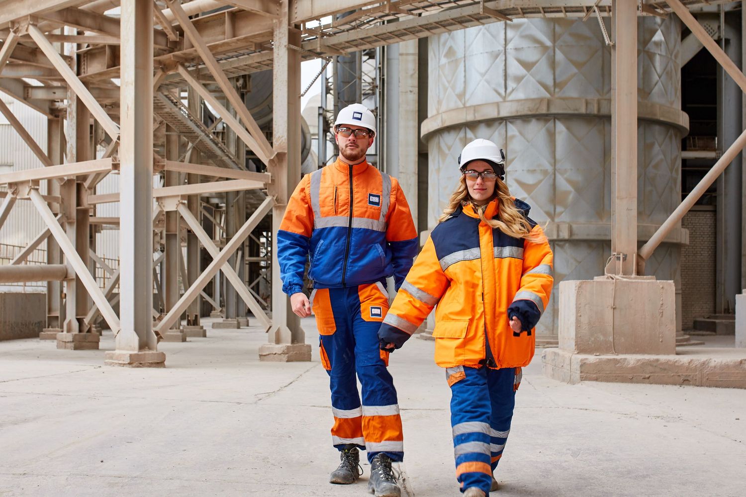 Two workers in hard hats and hi-vis walking through an industrial plant, photographed by RezinMedia