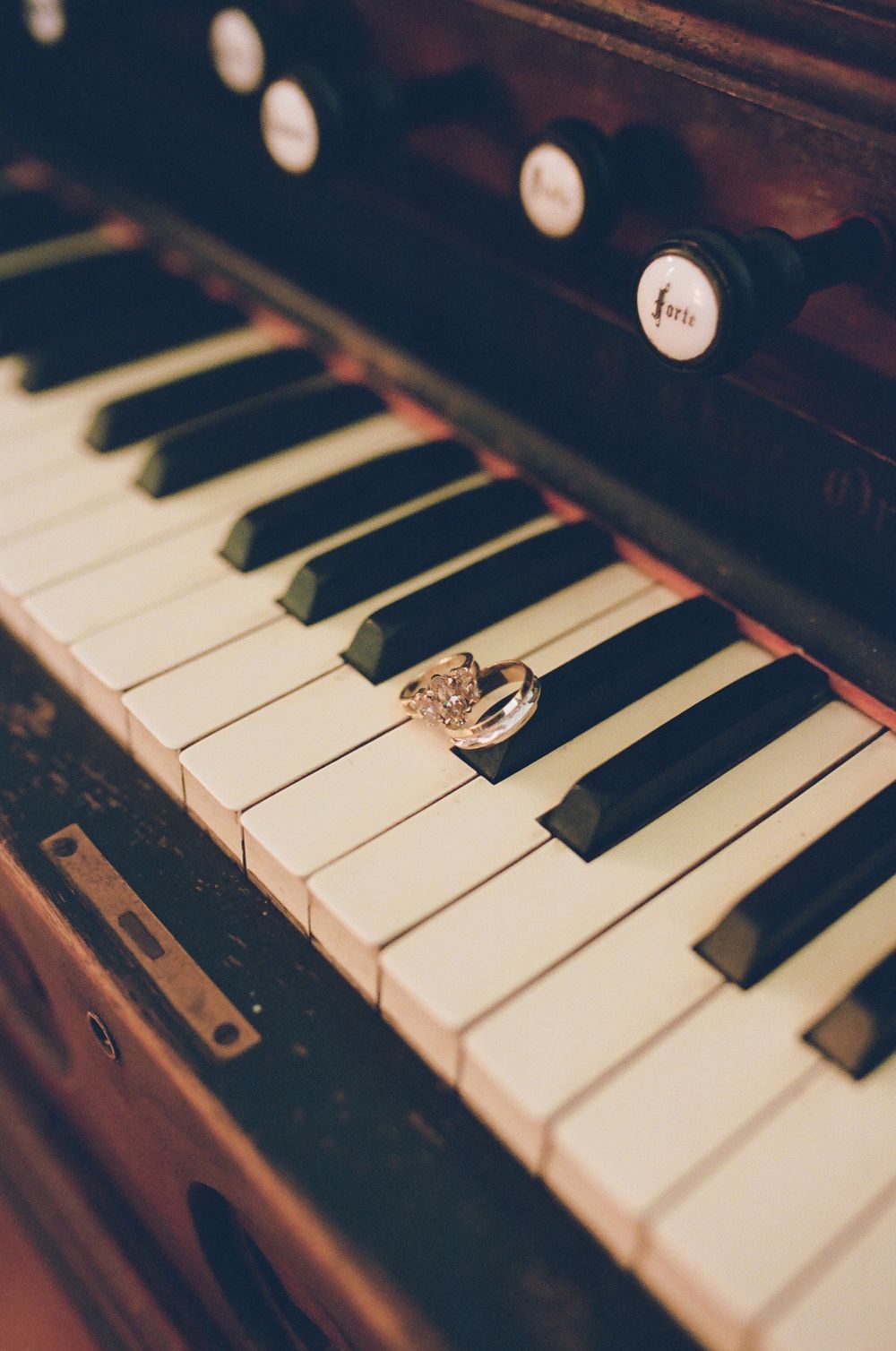 Two sparkling wedding rings rest on the ivory keys of a vintage reed organ with wooden stops and black keys.