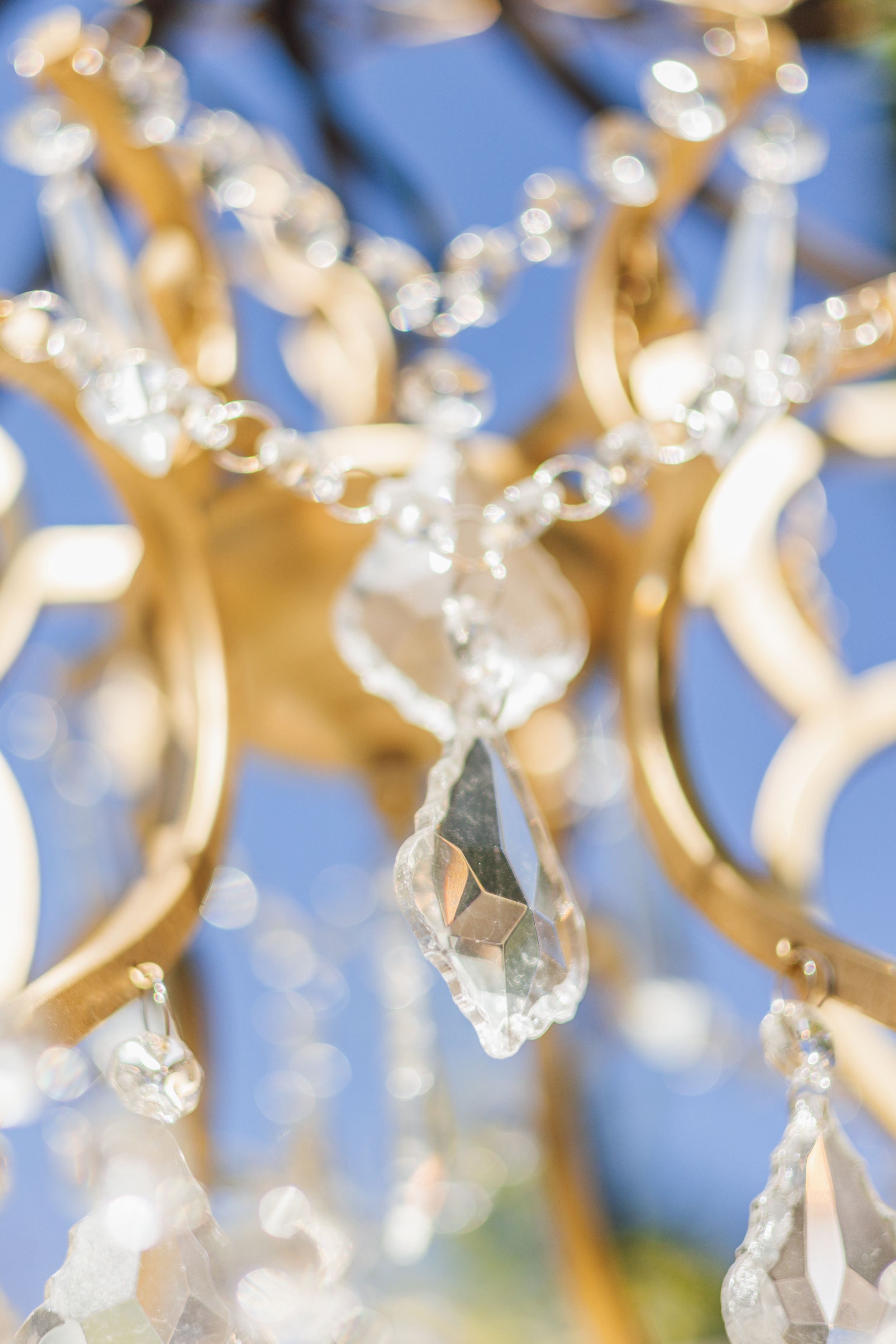 Close-up of elegant crystal chandelier pendants with gold frame details against a soft blue background.