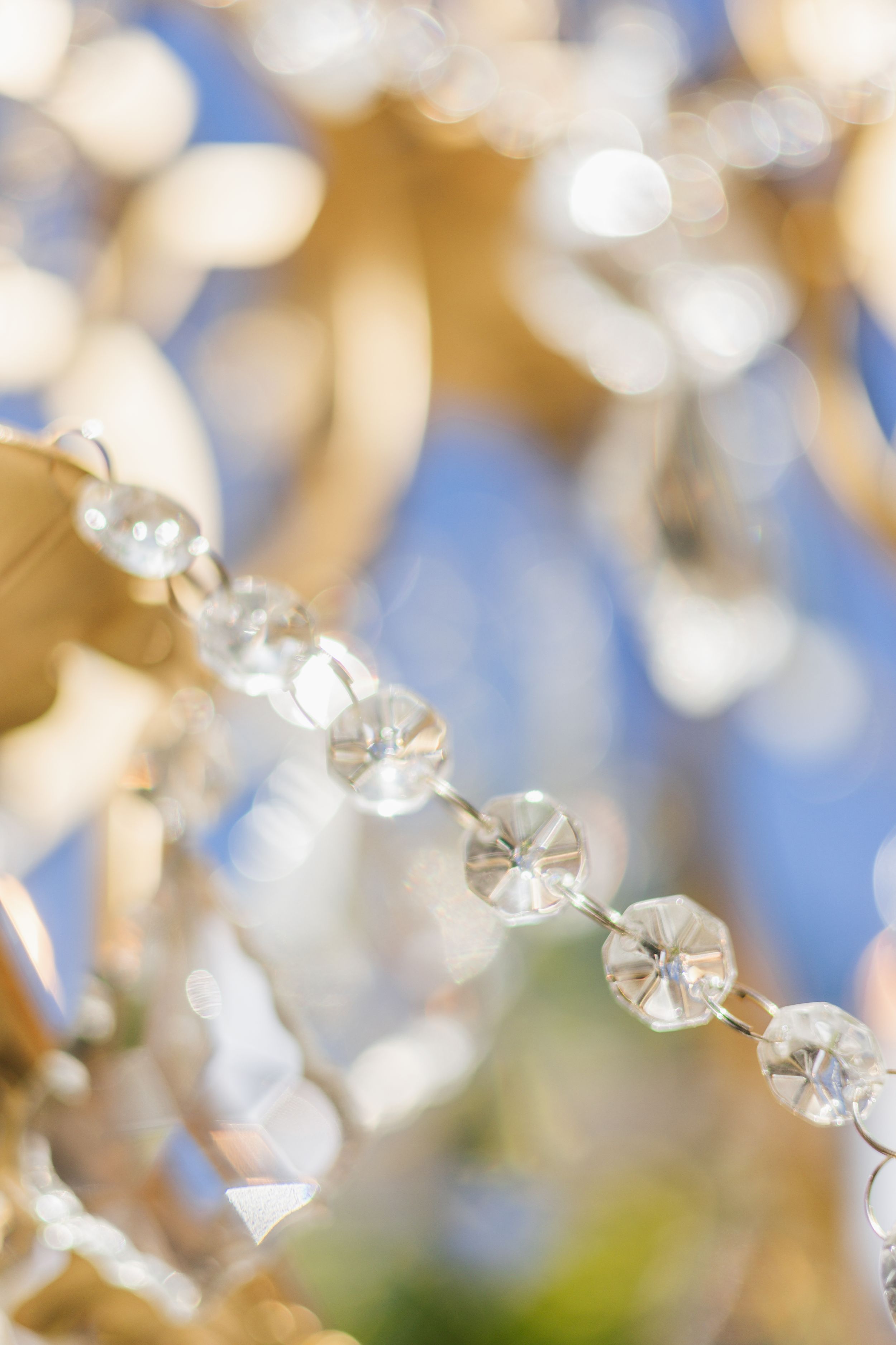 Close-up of sparkling crystal chandelier beads with golden brass frame and soft bokeh blue background.
