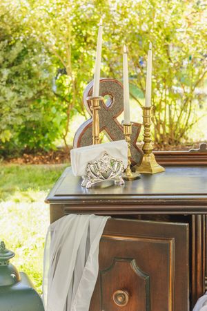 Elegant wedding display on antique wooden dresser with gold candlesticks, letter R, and decorative items outdoors.