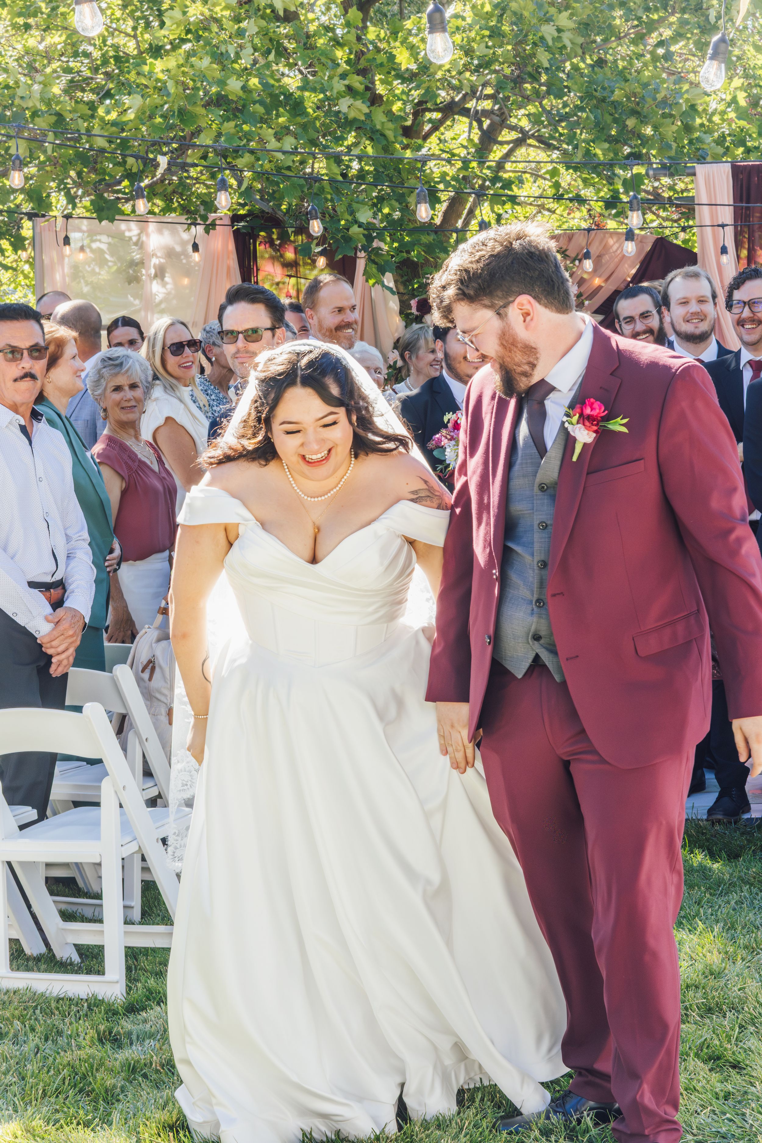 Bride and groom walk down the aisle, smiling joyfully, as guests celebrate their outdoor wedding ceremony.