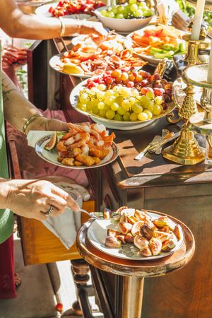 Elegant buffet table with fresh fruit platters, grapes, and bacon served at an outdoor catered event.