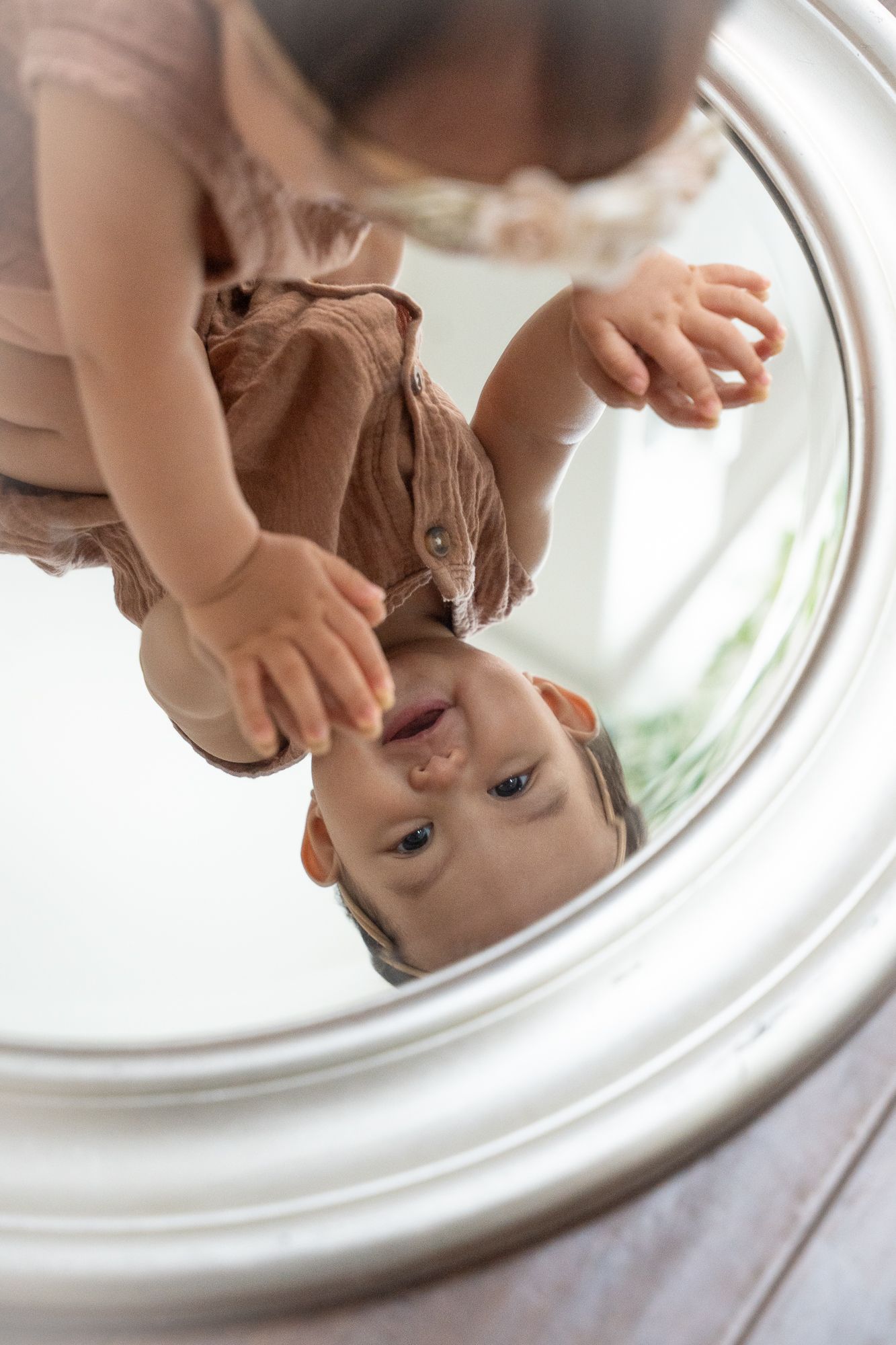 Baby reaching toward their reflection in a round mirror.