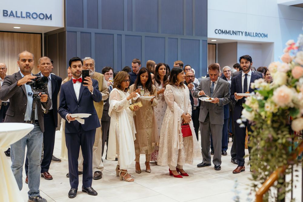 Guests in elegant formal attire gather near the ballroom entrance at an event, with a floral arrangement in the foreground.