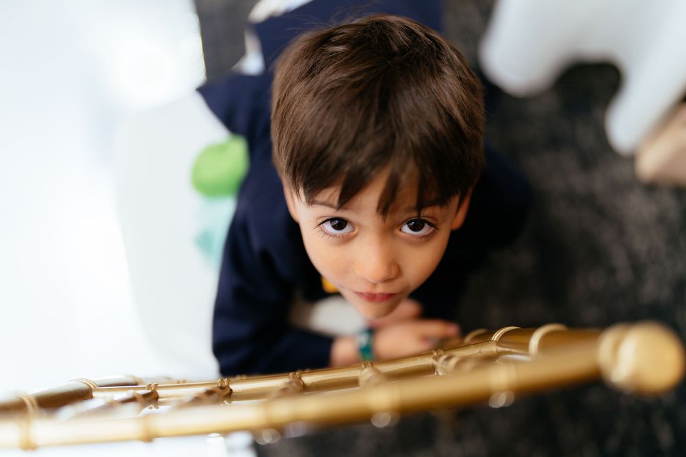 Young boy with brown hair in a navy outfit looks up at the camera while resting his hands on a gold railing.