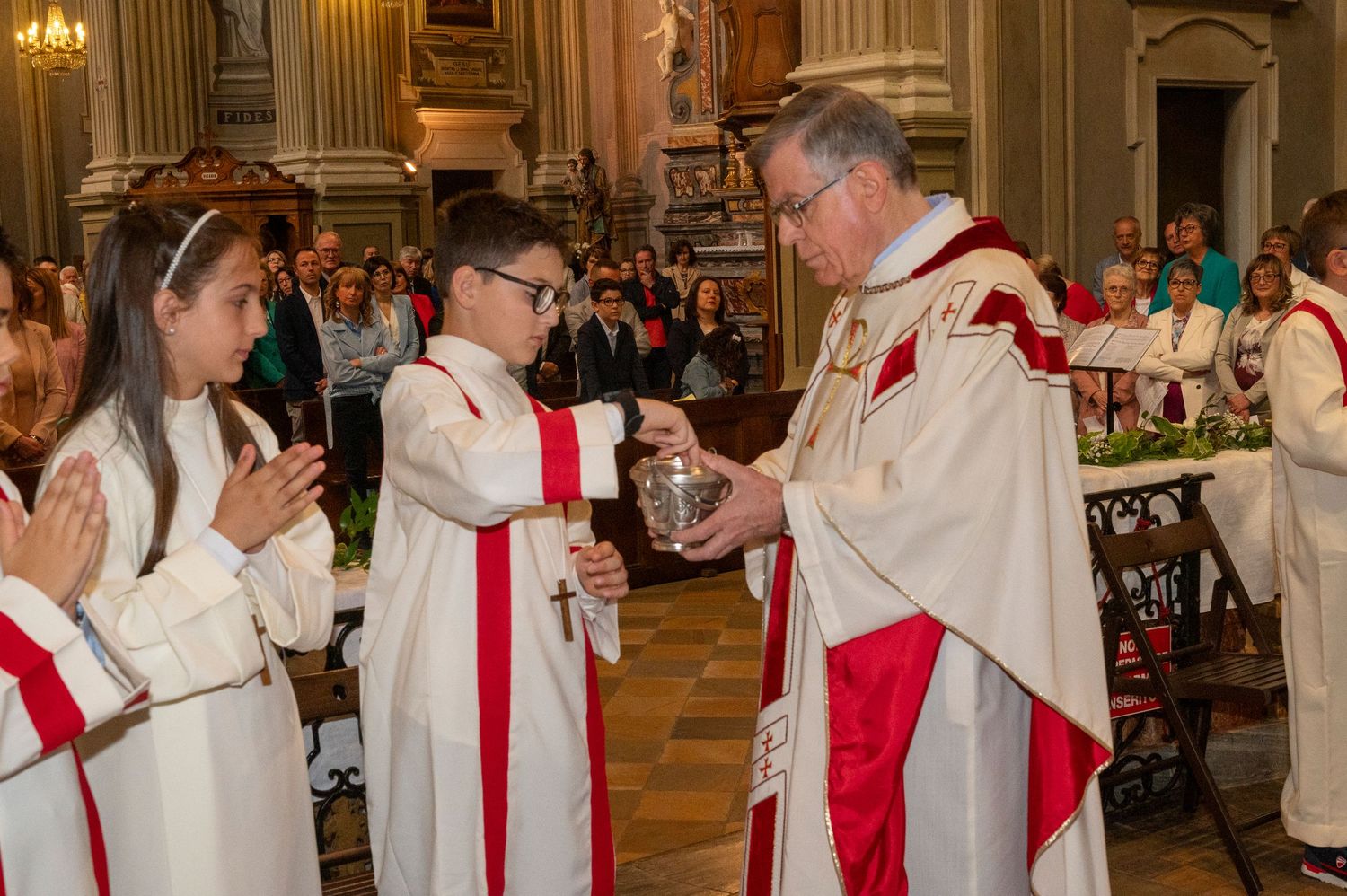 Religious ceremony in an ornate church with clergy in traditional red and white vestments.