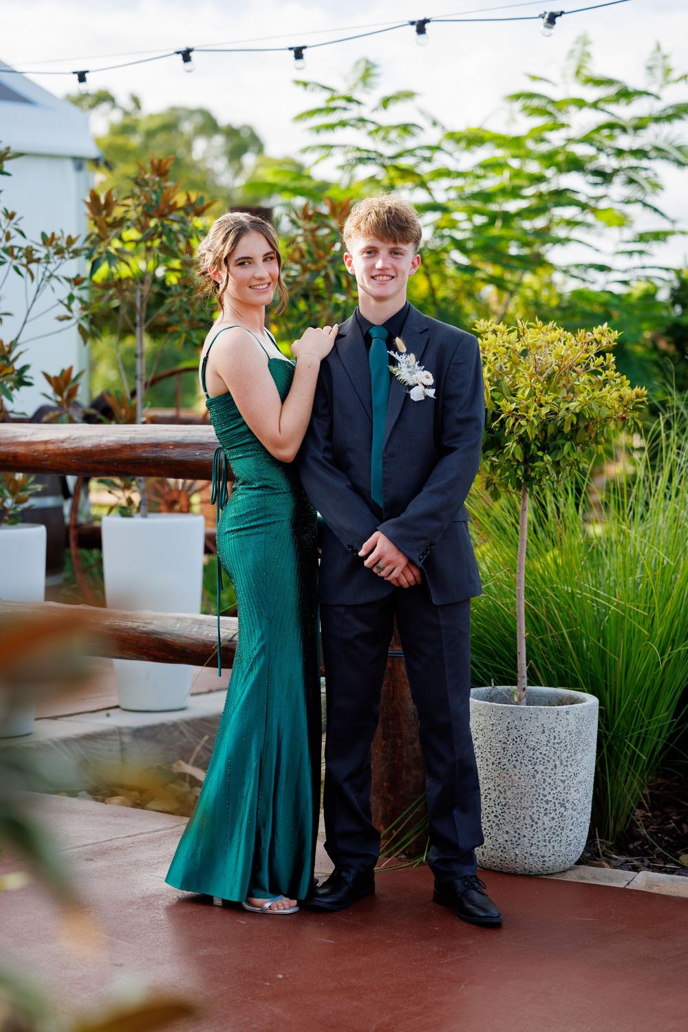 Smiling teen couple posing for formal photos, the girl in a green satin gown and the boy in a dark suit with a corsage.
