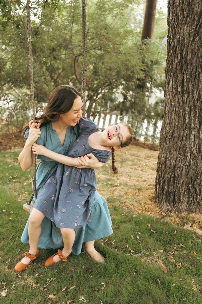 A mother and daughter laugh together on a tree swing in a lush backyard at Beverly Harris House in downtown McKinney TX