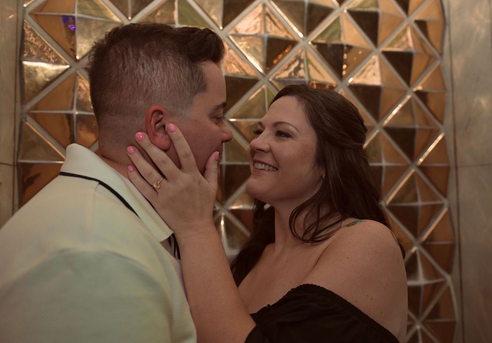 Couple sharing an intimate moment smiling at each other against a decorative mirror wall.
