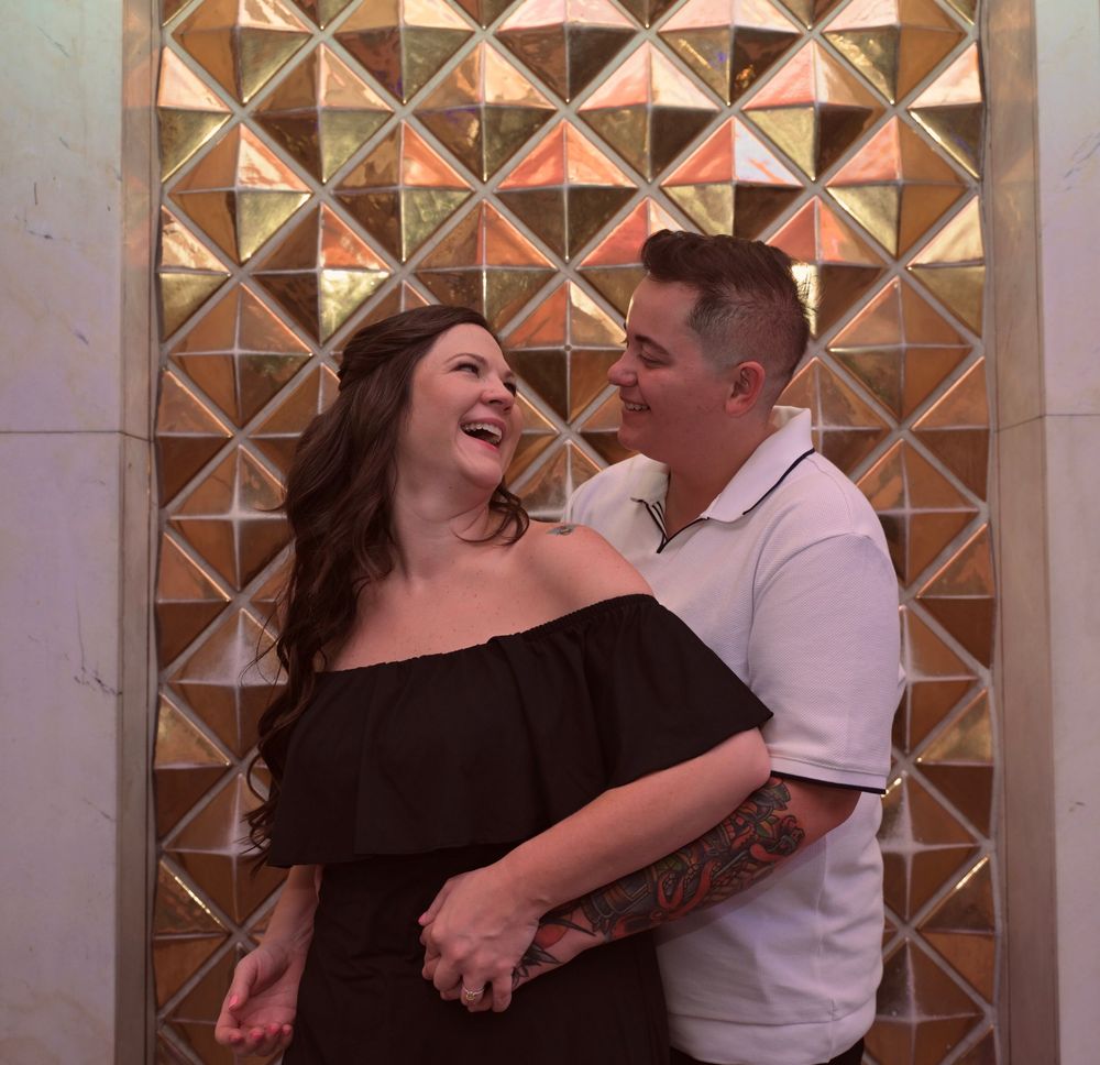 Happy couple laughing together in front of a golden geometric decorative wall backdrop.