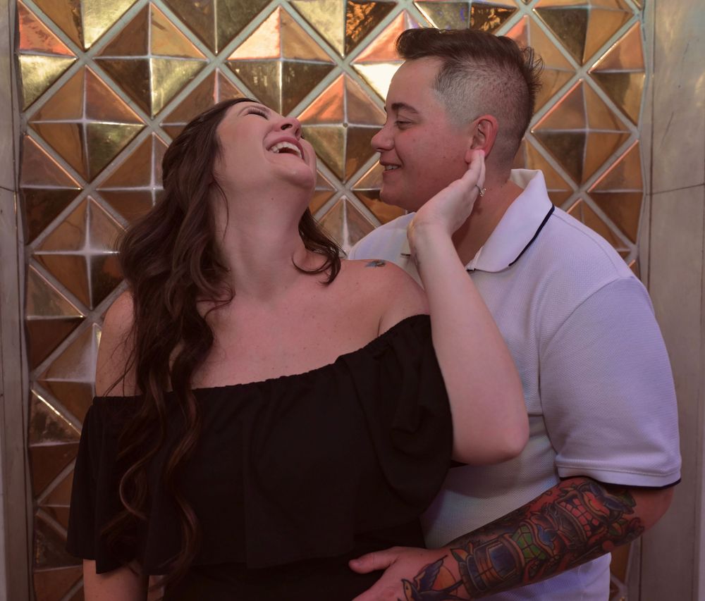 Laughing couple in a tender embrace against a gold geometric mirrored wall.
