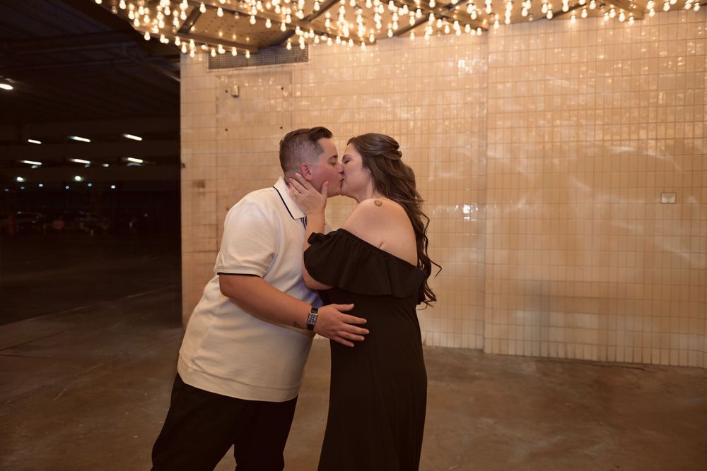 Couple sharing a romantic kiss under warm string lights in an elegant venue with a gold shimmer wall backdrop.