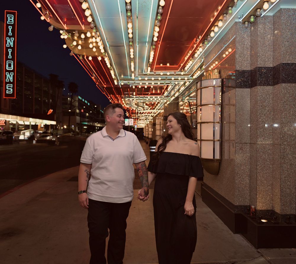 Couple holding hands walking past Binions casino at night under colorful neon lights in Las Vegas.