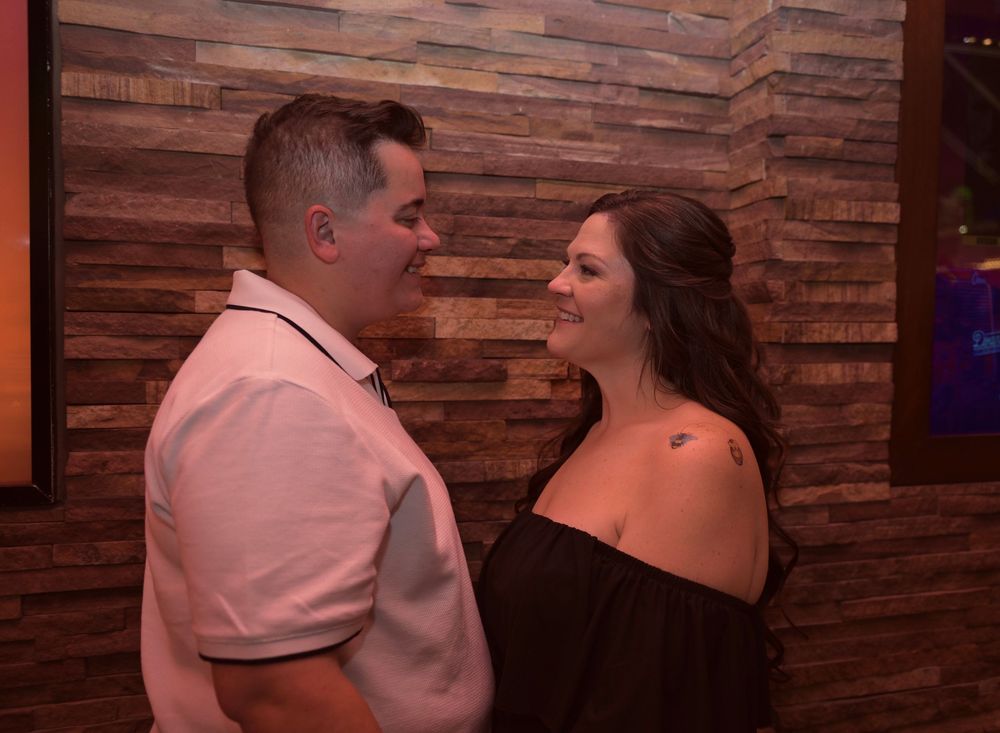 Couple sharing a romantic moment, smiling at each other in front of a wooden wall backdrop.