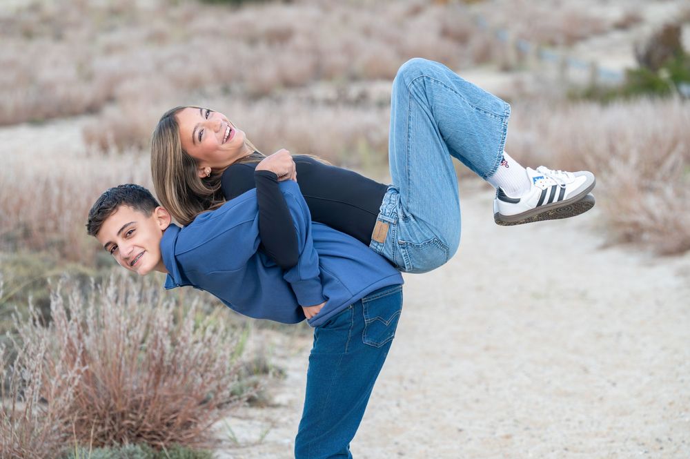Young couple playfully posing outdoors, man carrying woman on his back on a sandy desert trail.