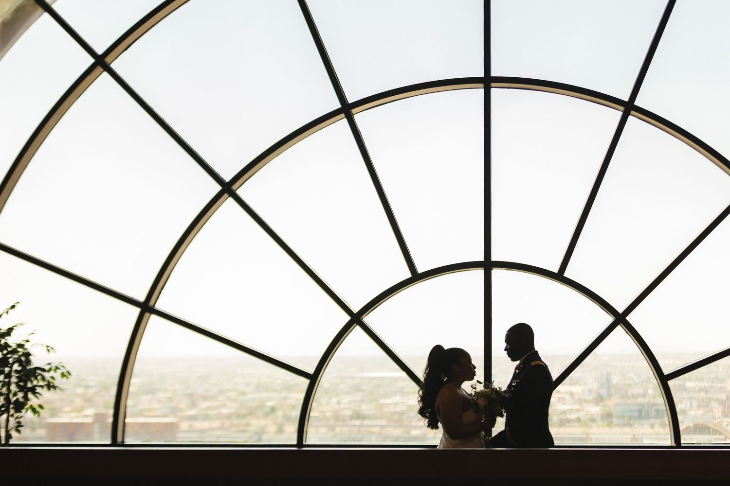 Wedding couple silhouetted beneath a large arched window overlooking the city.