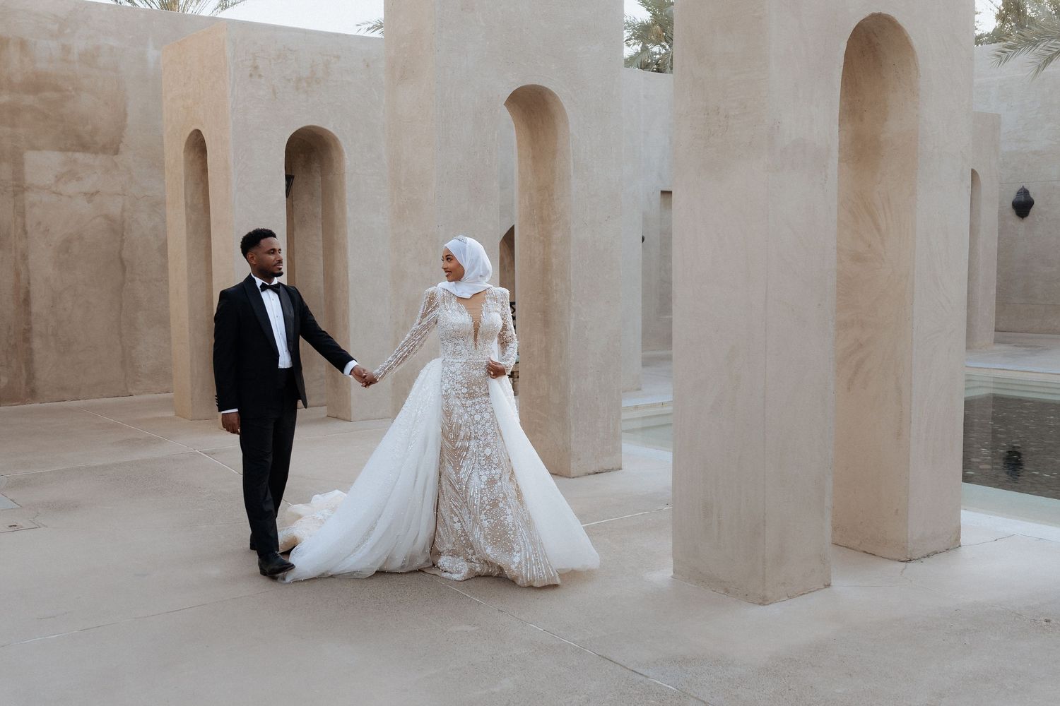 Couple holding hands as they walk between tall sandstone arches at a Dubai wedding shoot