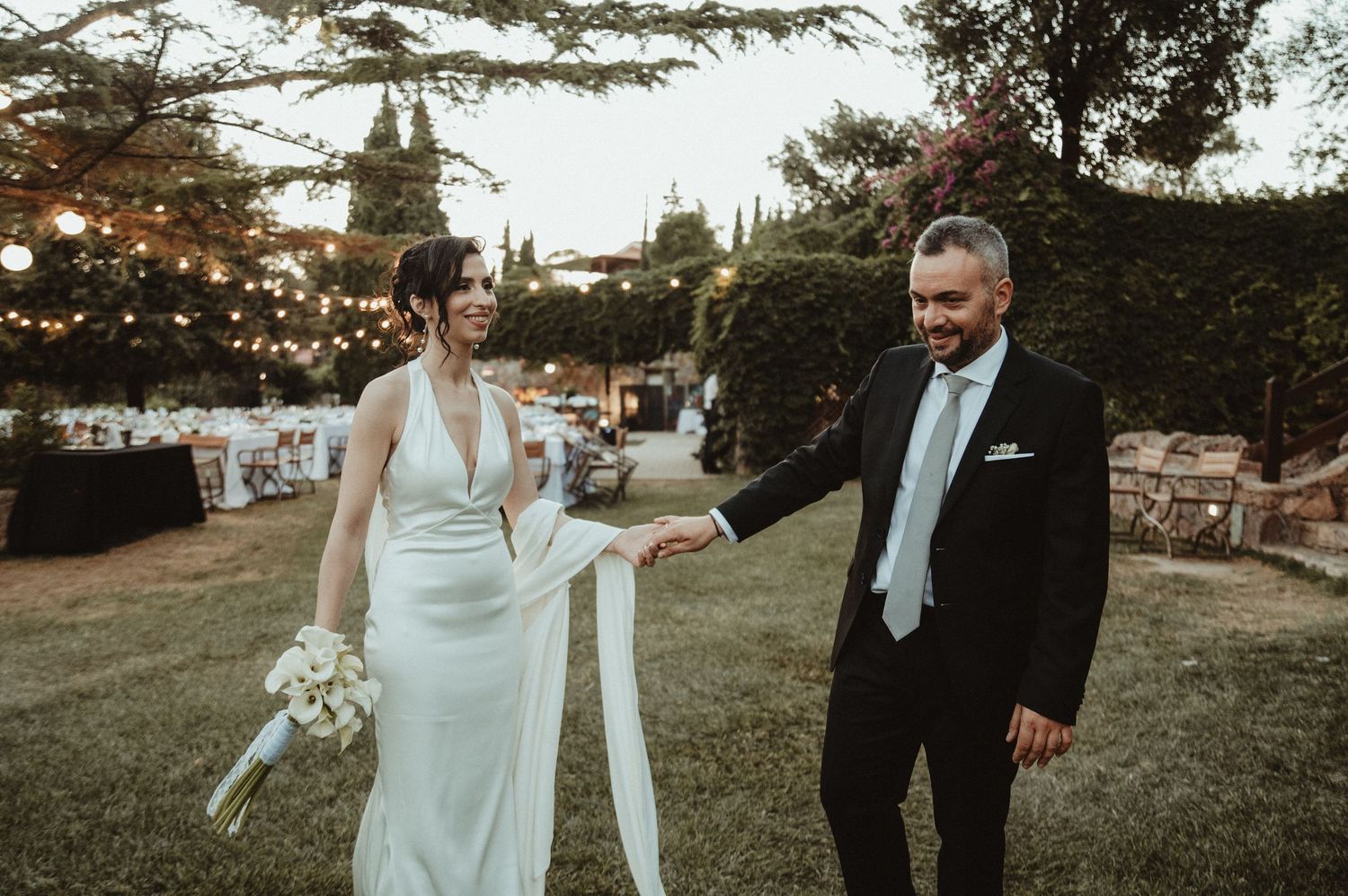 Black and white wedding photo of bride and groom gazing at each other outdoors among trees.