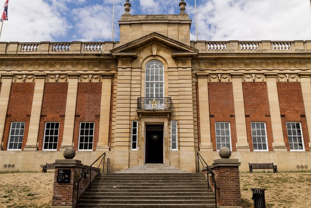 Grand brick and stone wedding venue exterior with classical columns, arched window, and sweeping entrance steps under blue sky.