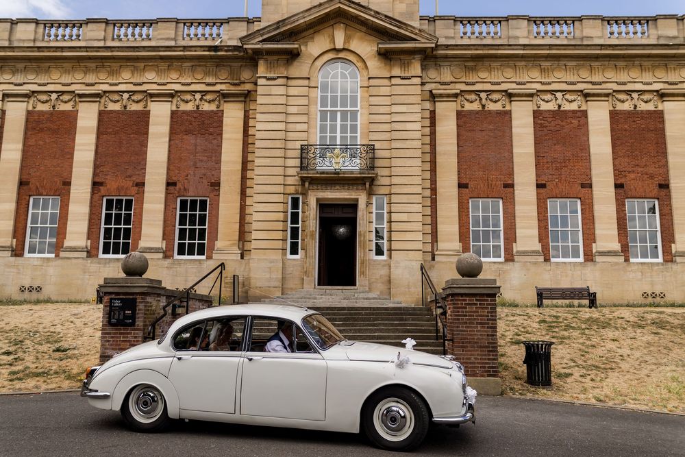 White vintage wedding car parked outside a grand brick building with stone steps.