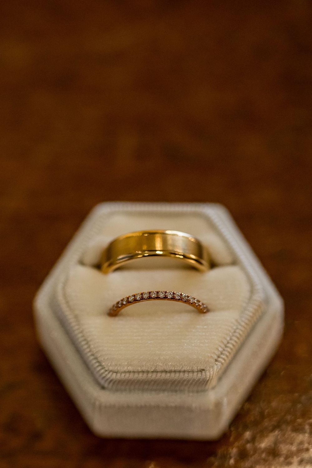 Two gold wedding rings displayed in a white hexagonal velvet ring box on a wooden surface.