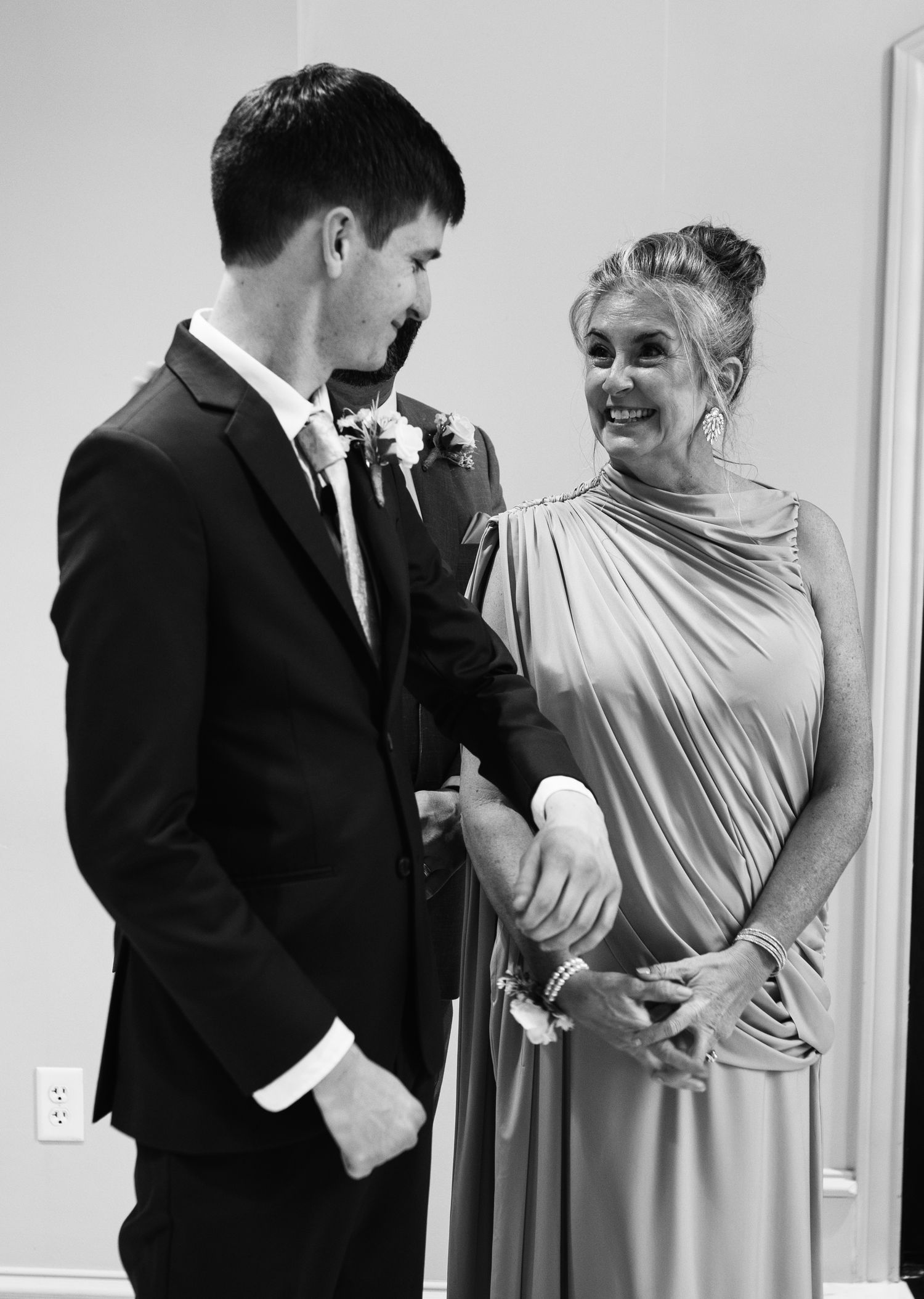 Black and white photo of a young man in a suit and a smiling woman in an elegant gown at a wedding ceremony.