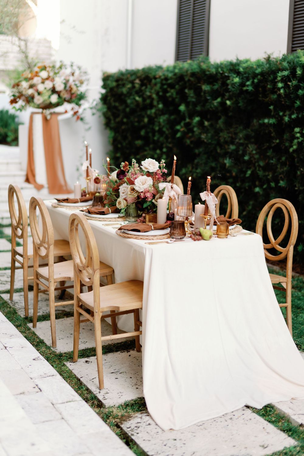 Elegant outdoor wedding reception table with copper accents, floral centerpieces, and wooden chairs.