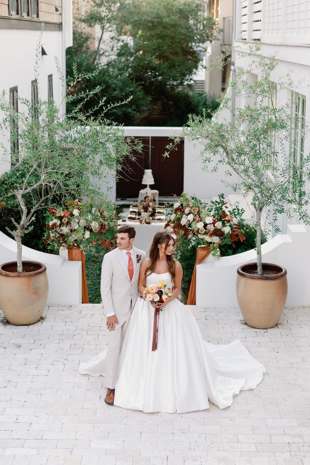 Bride and groom stand in elegant white courtyard with terracotta planters and lush floral arrangements at The Pearl Hotel.
