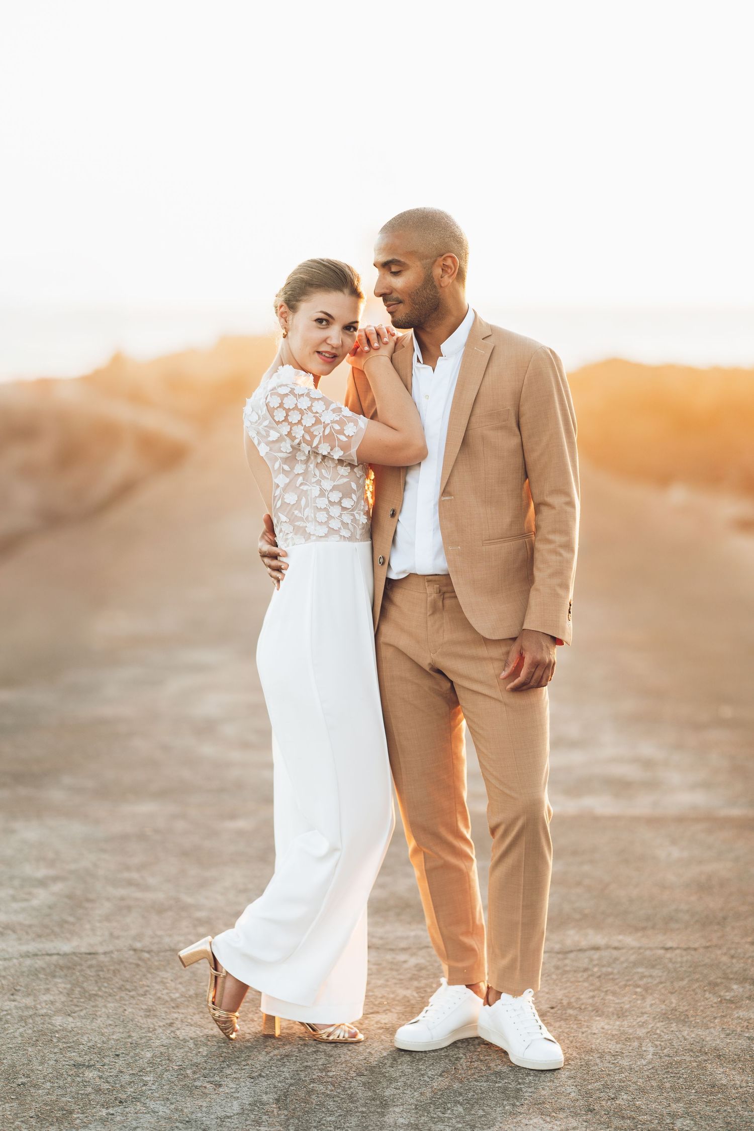 Happy couple in wedding attire laughing together outdoors with tropical palm trees in the background.