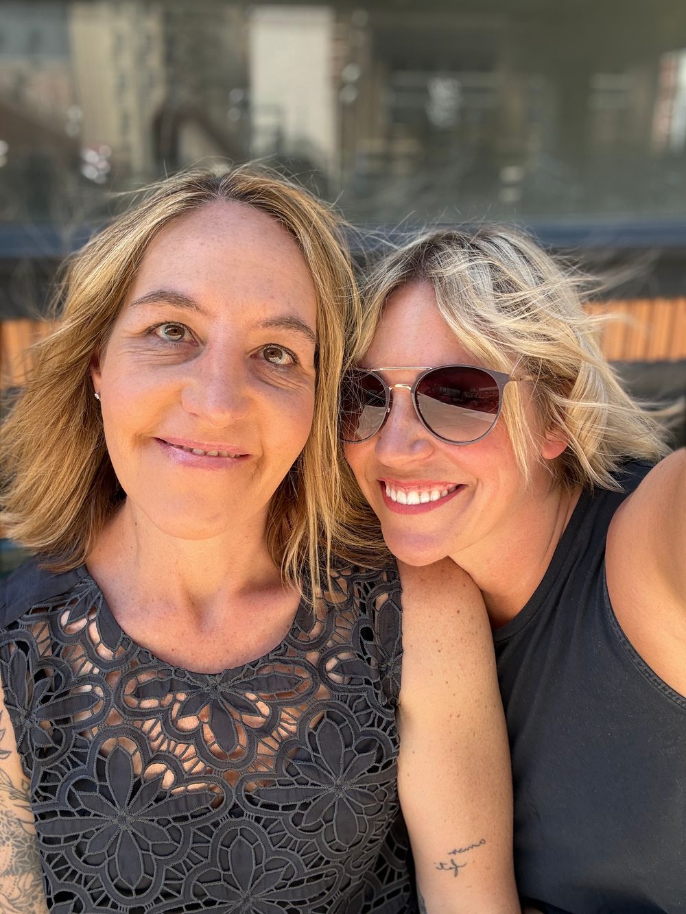 Two smiling women with blonde hair pose together outdoors for a cheerful selfie on a sunny day.