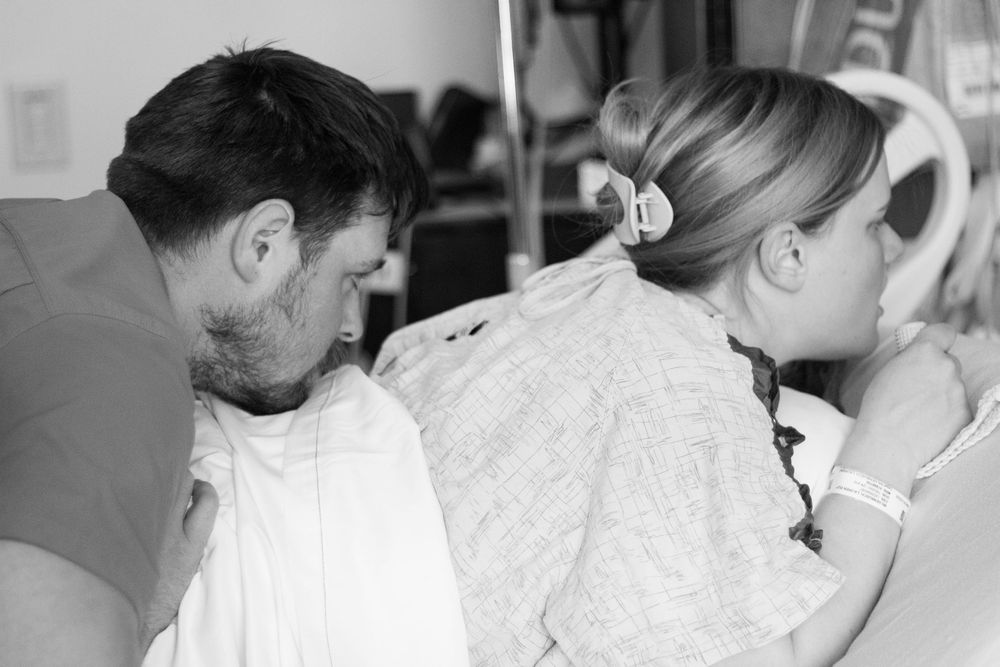 Couple sharing tender moment during labor in hospital room black white.