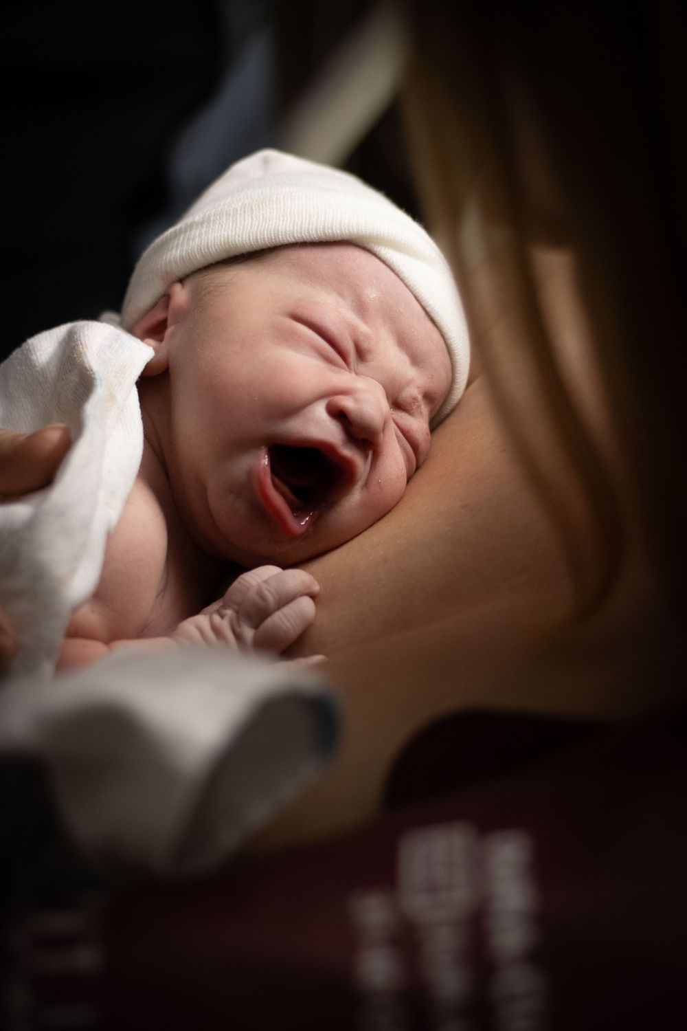 Newborn baby yawning while being held by mother after birth.