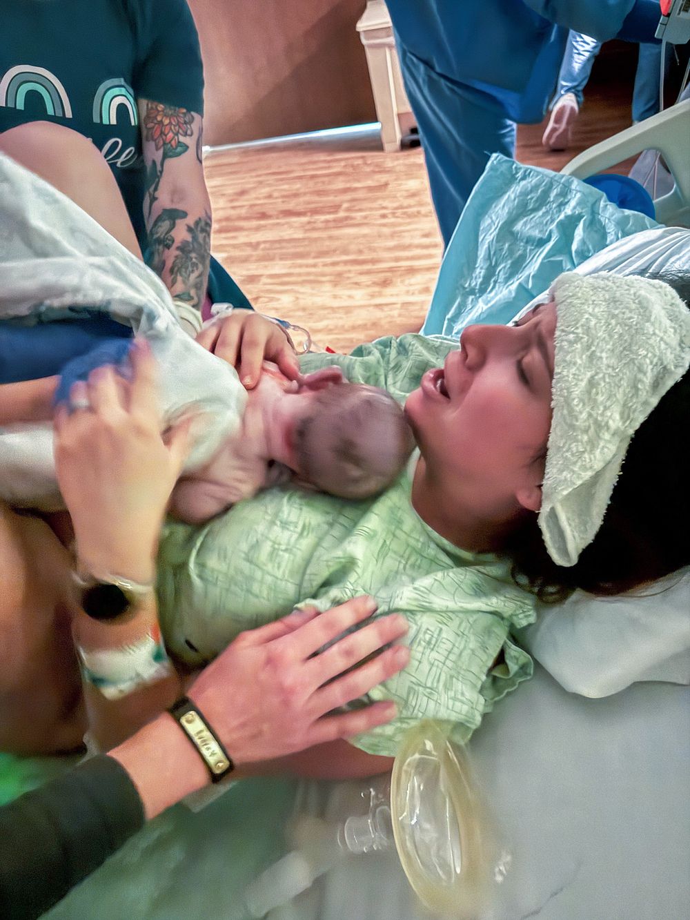 Mother holds her newborn baby skin-to-skin immediately after delivery in a hospital bed.
