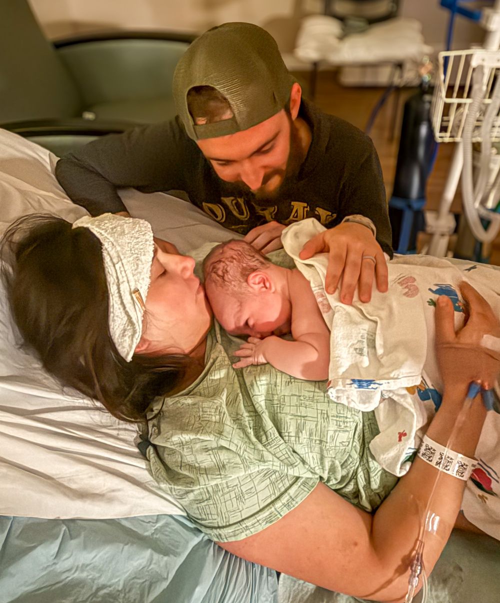 New parents sharing first moments with newborn baby in hospital bed.