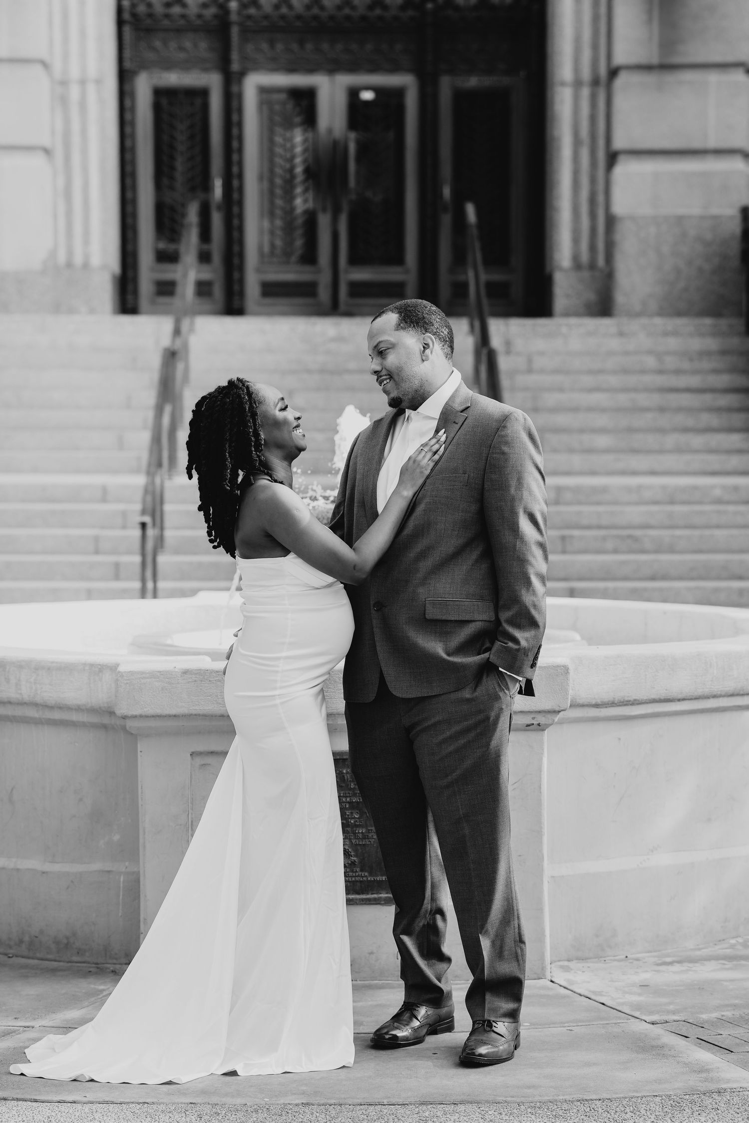 Black and white photo of a bride and groom sharing a romantic moment on steps outside a grand building.