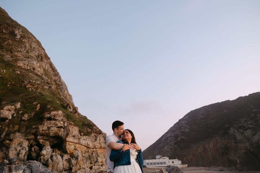 Couple embracing romantically at dusk with dramatic rocky cliffs and mountains in the background.