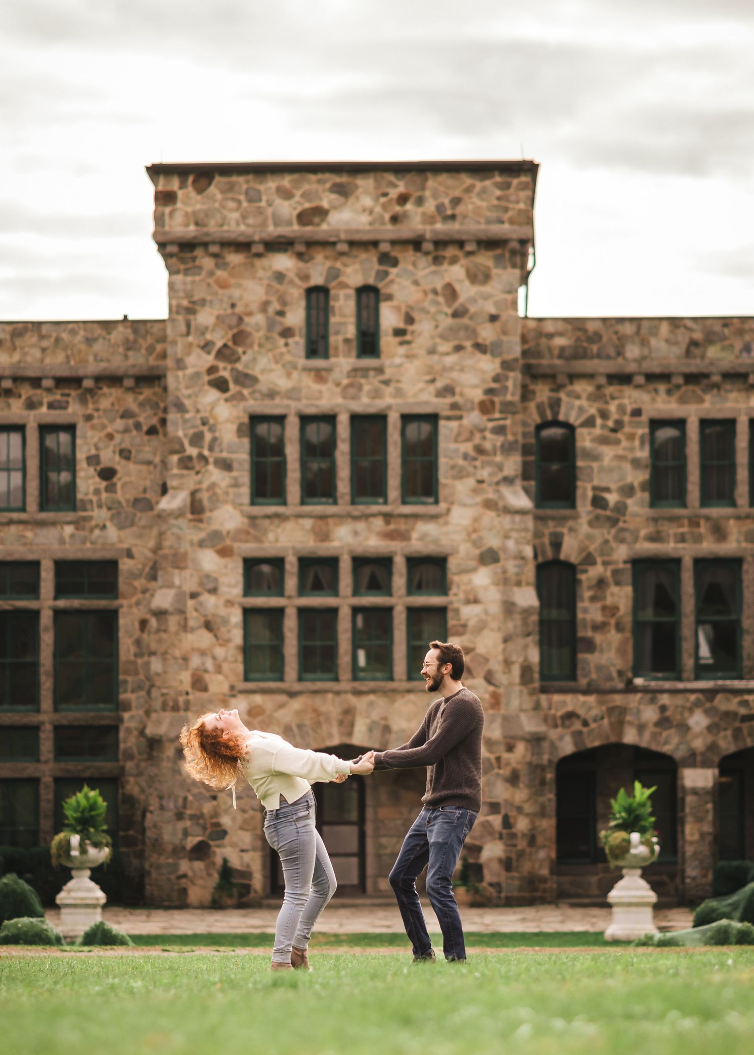 Engaged couple laughing mid-dance dip in front of the historic stone Ames Mansion at Borderland State Park, her hair caught in motion.