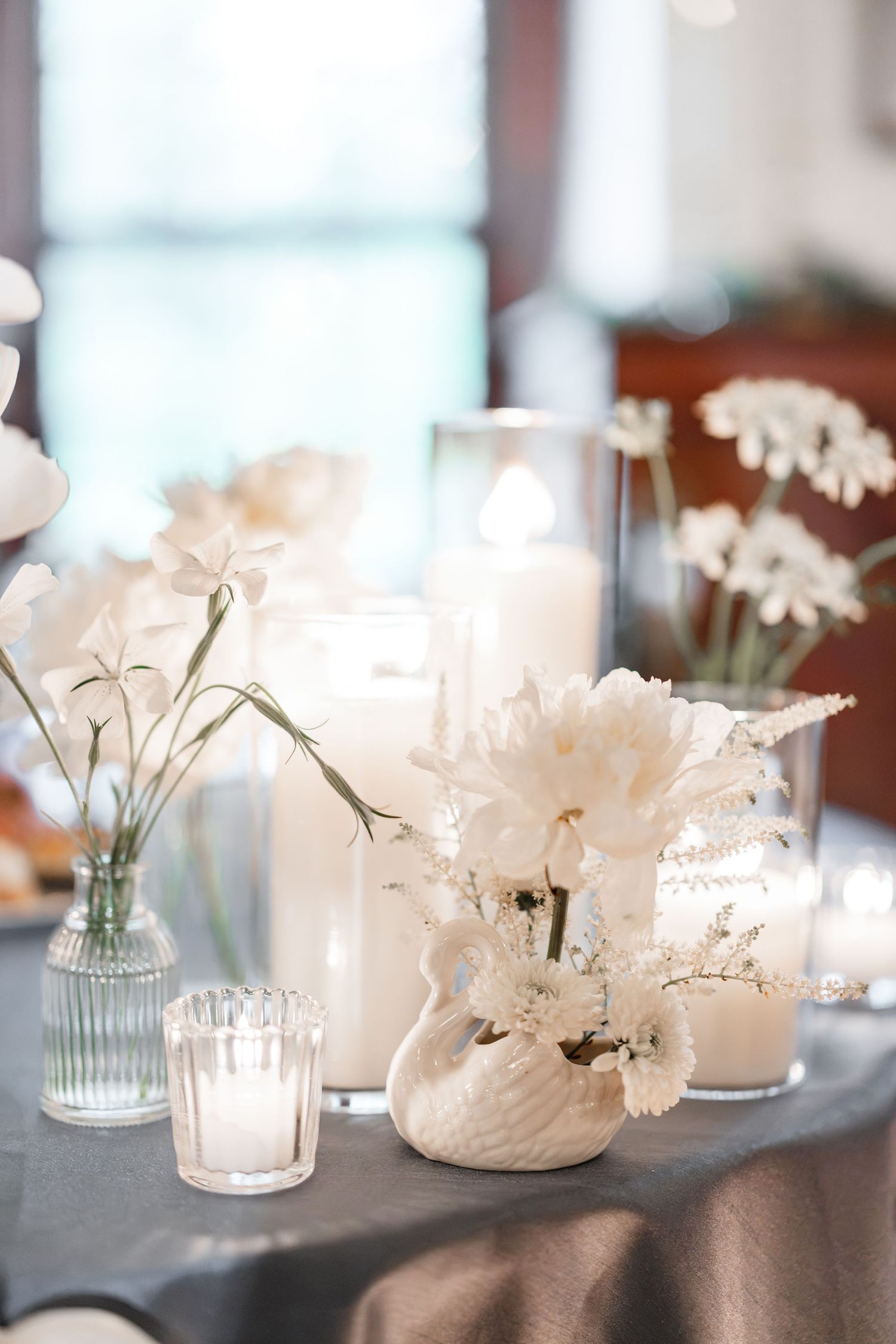 Elegant wedding centerpiece with white flowers, pillar candles, and a swan vase.