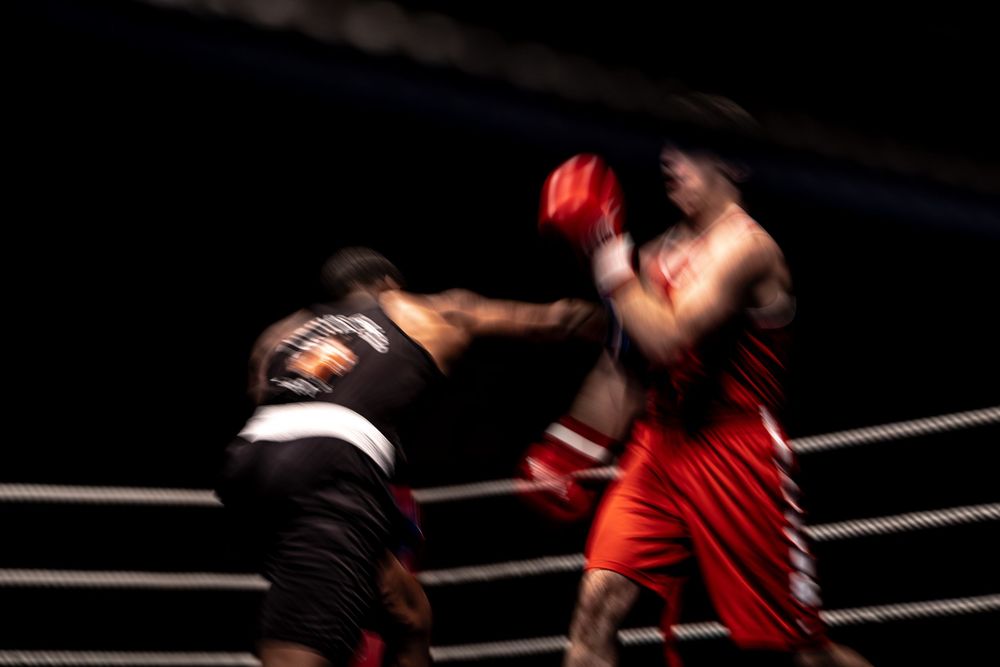 Two boxers exchange punches in a dynamic motion-blurred action shot inside a boxing ring.