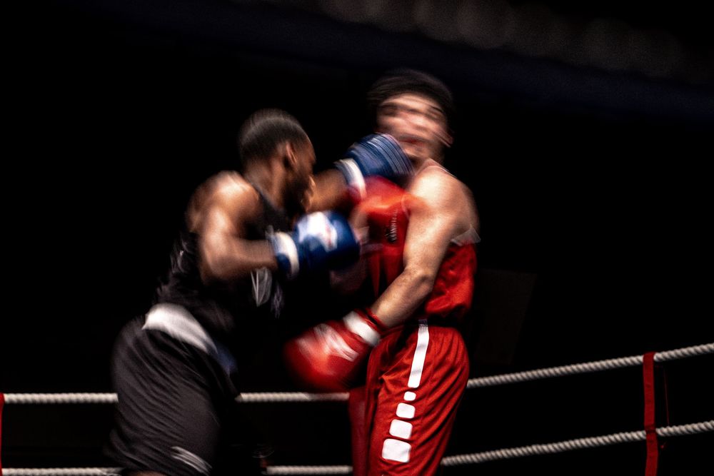 Two boxers exchange punches in a dynamic motion-blurred action shot inside a boxing ring.